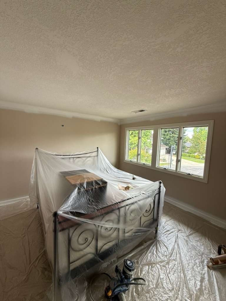 Bedroom furniture wrapped in protective plastic and floors fully covered with tarps before painting begins. Alliance Trio Solutions on-site prep