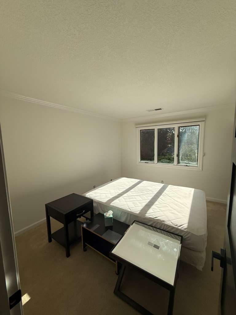 Bright residential bedroom after a full repaint with warm off-white walls and clean trim, natural light through the window